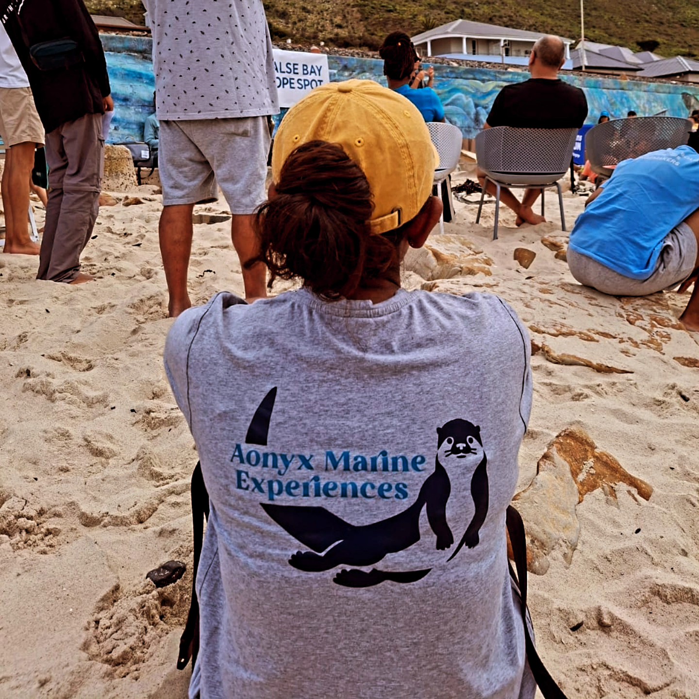 An Aonyx guide in a branded shirt at a False Bay Hope Spot gathering on the sand
