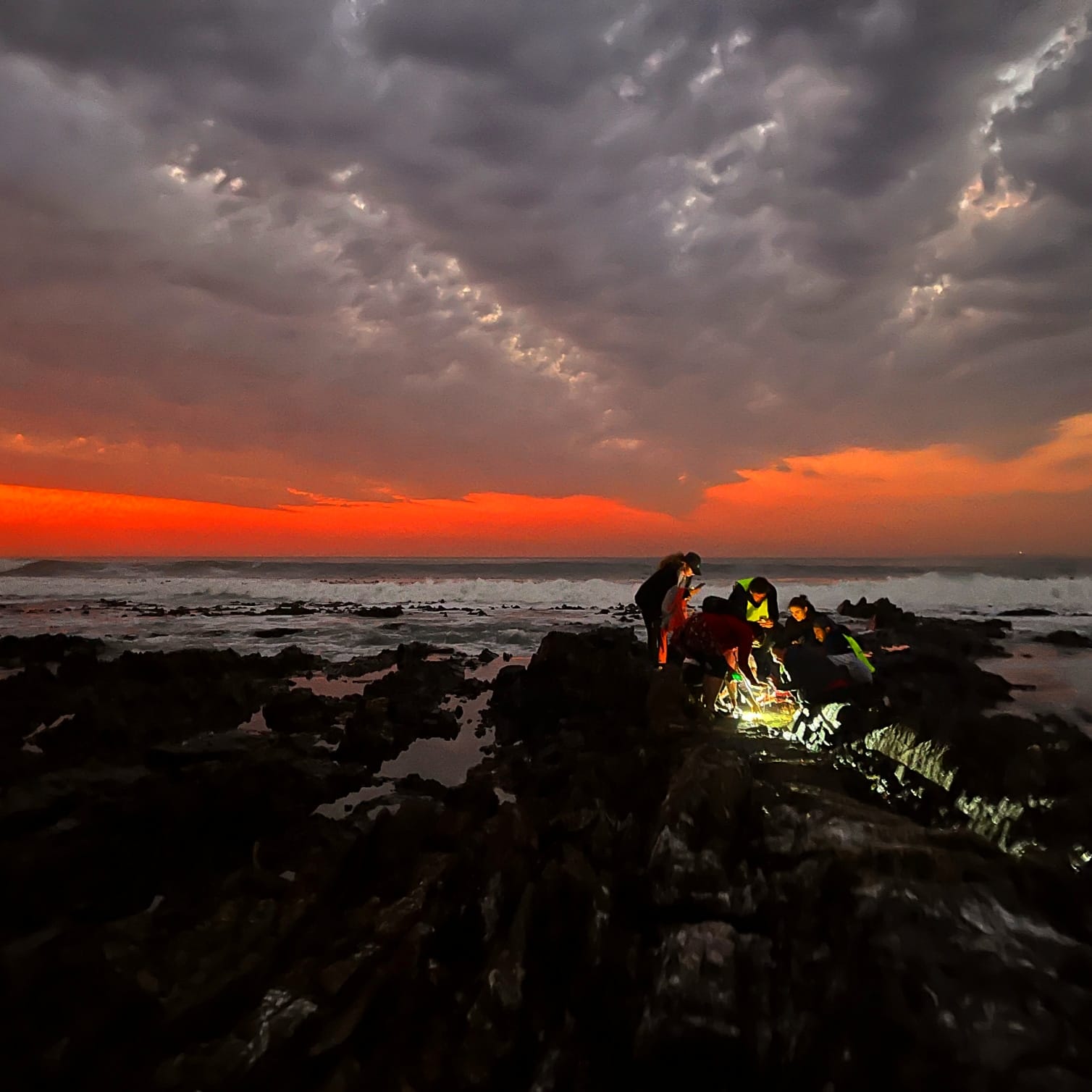 Torchlight on the rocks as the sun sets behind heavy cloud and surf