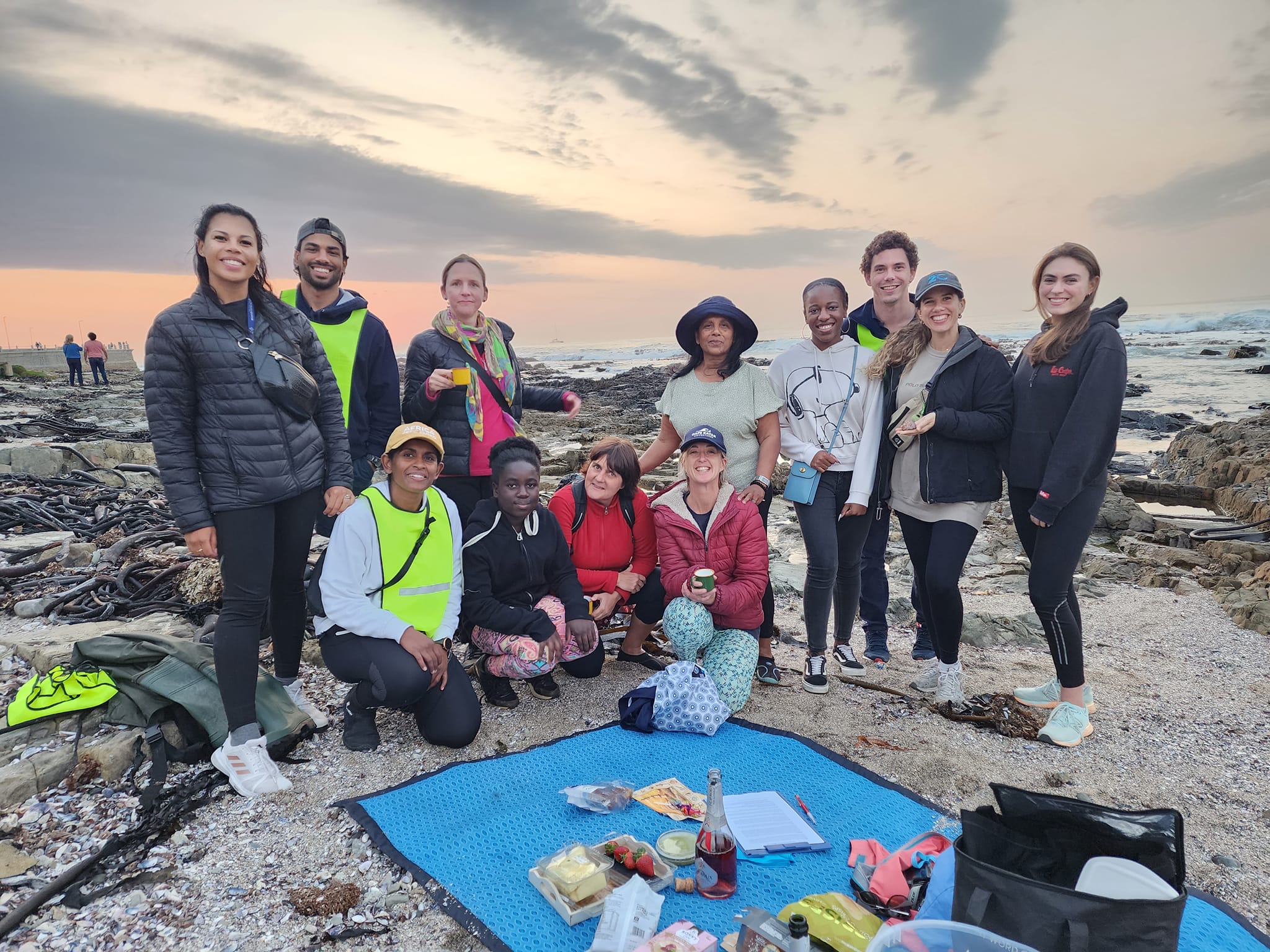 The group together on the shore at sunset with snacks laid out at the end of a walk